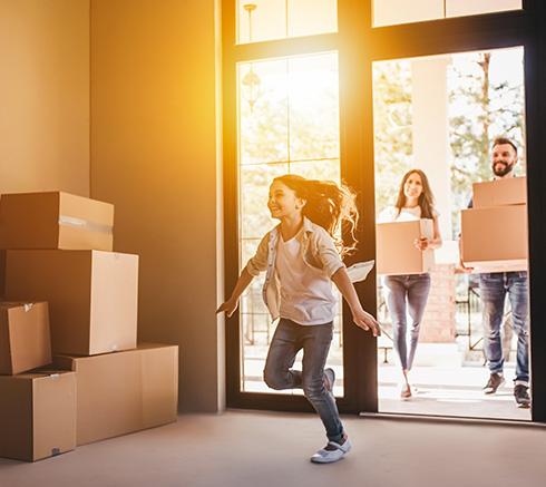 child running into new home, parents carry moving boxes